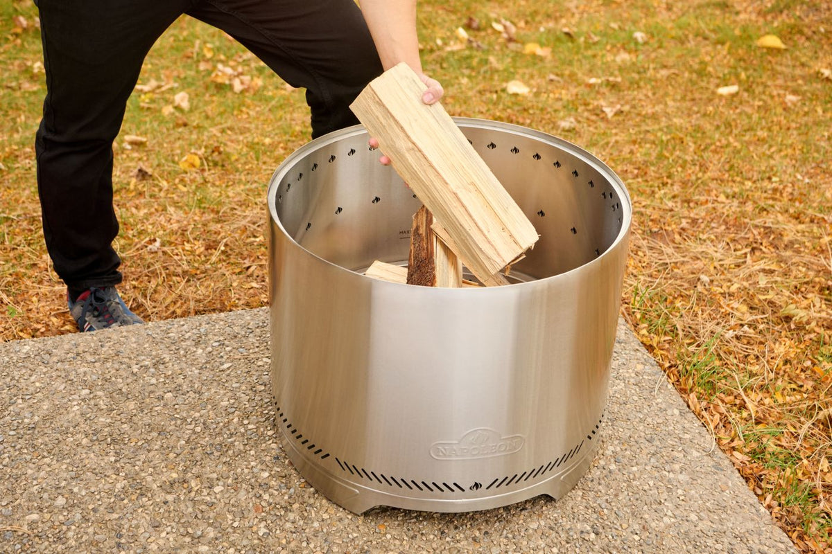 Napoleon Timberwolf 18-inch stainless steel smokeless fire pit being loaded with firewood
